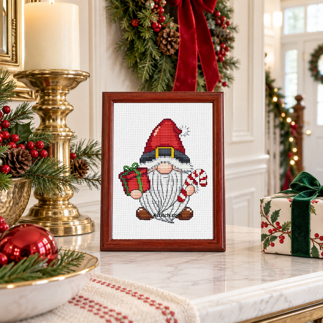 Santa Belt Gnome, featuring a Santa-belt hat gnome with a red-and-green gift and a candy cane, on continuous white Aida in a small tabletop frame in a bright Christmas interior.
