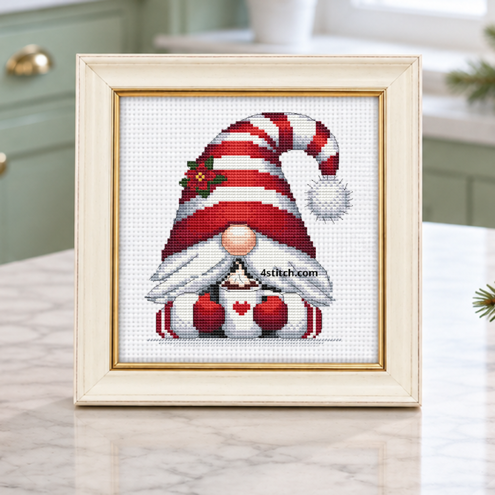 Heart Mug Christmas Gnome with a red-and-white striped hat with holly and a white heart mug filled with hot cocoa, on white Aida in an ivory and gold frame on a light Christmas cocoa station.