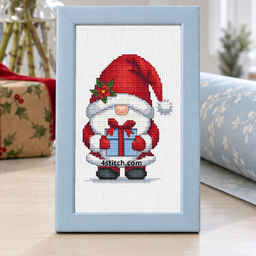 Christmas Present Gnome with a tall holly-trimmed Santa hat and a blue present tied with a red bow, on white Aida in a powder-blue frame in a sunny Christmas wrapping nook.