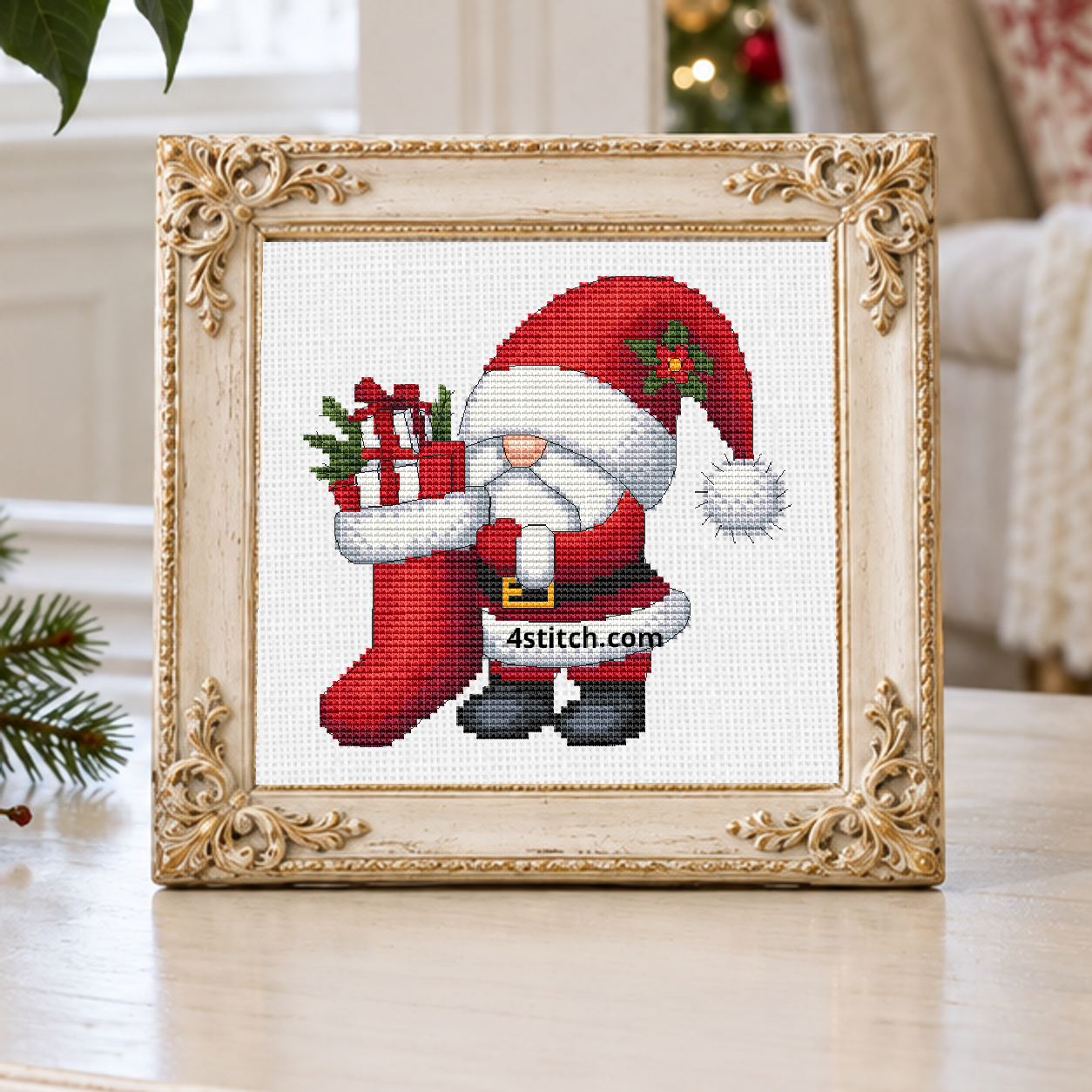 Christmas Stocking Santa Gnome with a holly-trimmed Santa hat and a long red stocking filled with wrapped presents, on white Aida in an ivory carved frame on a bright festive sideboard.