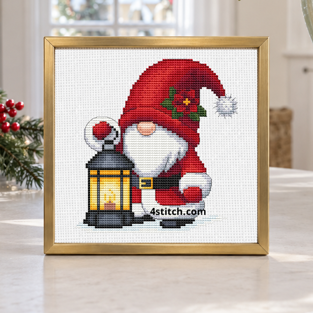 Christmas Lantern Santa Gnome with a holly-decorated red Santa hat and a lantern with a golden light, on white Aida in a brushed brass frame on a bright winter entrance table.