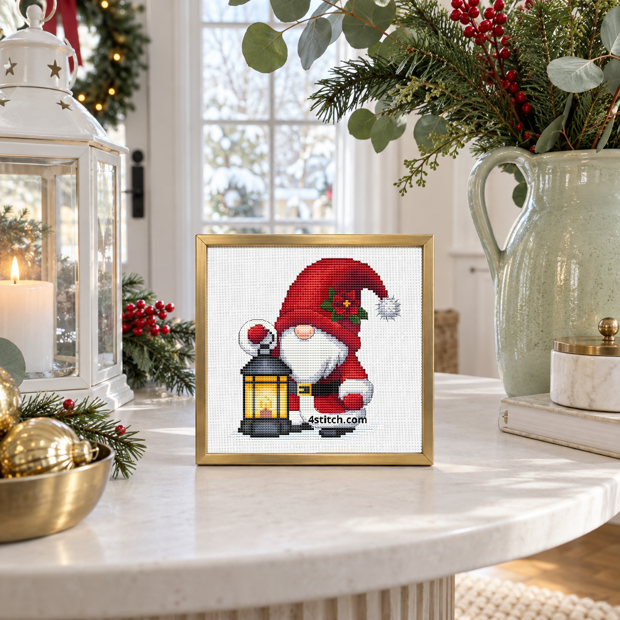 Christmas Lantern Santa Gnome with a holly-decorated red Santa hat and a lantern with a golden light, on white Aida in a brushed brass frame on a bright winter entrance table.