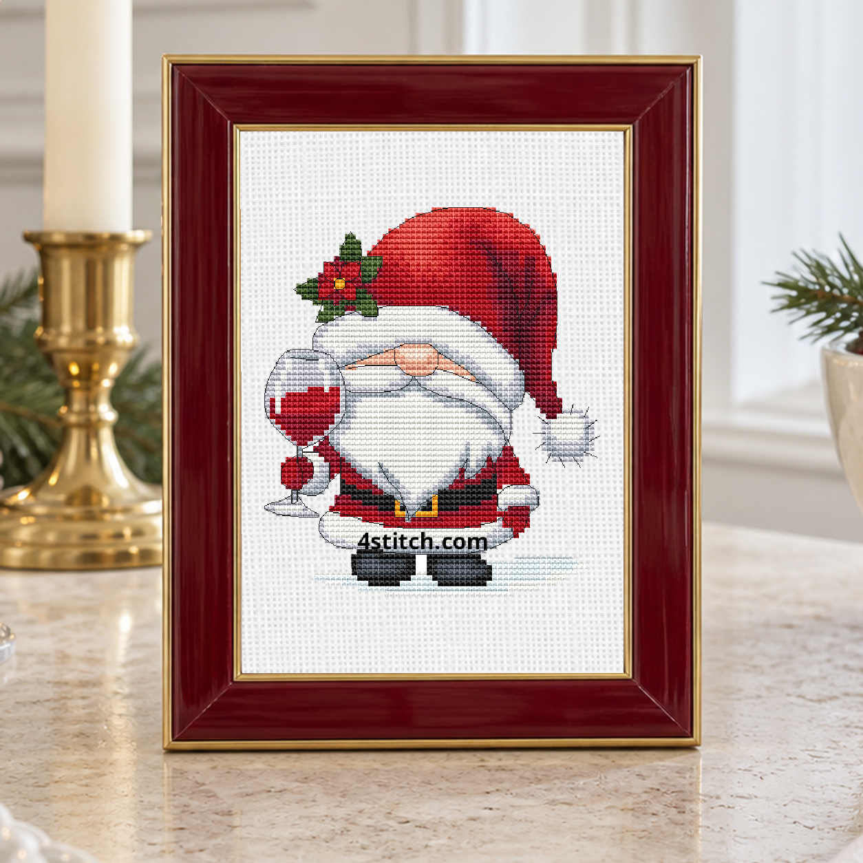 Wine Glass Santa Gnome with a red Santa hat with holly and a stemmed glass of red wine, on white Aida in a burgundy-and-gold frame on a bright Christmas dining console.