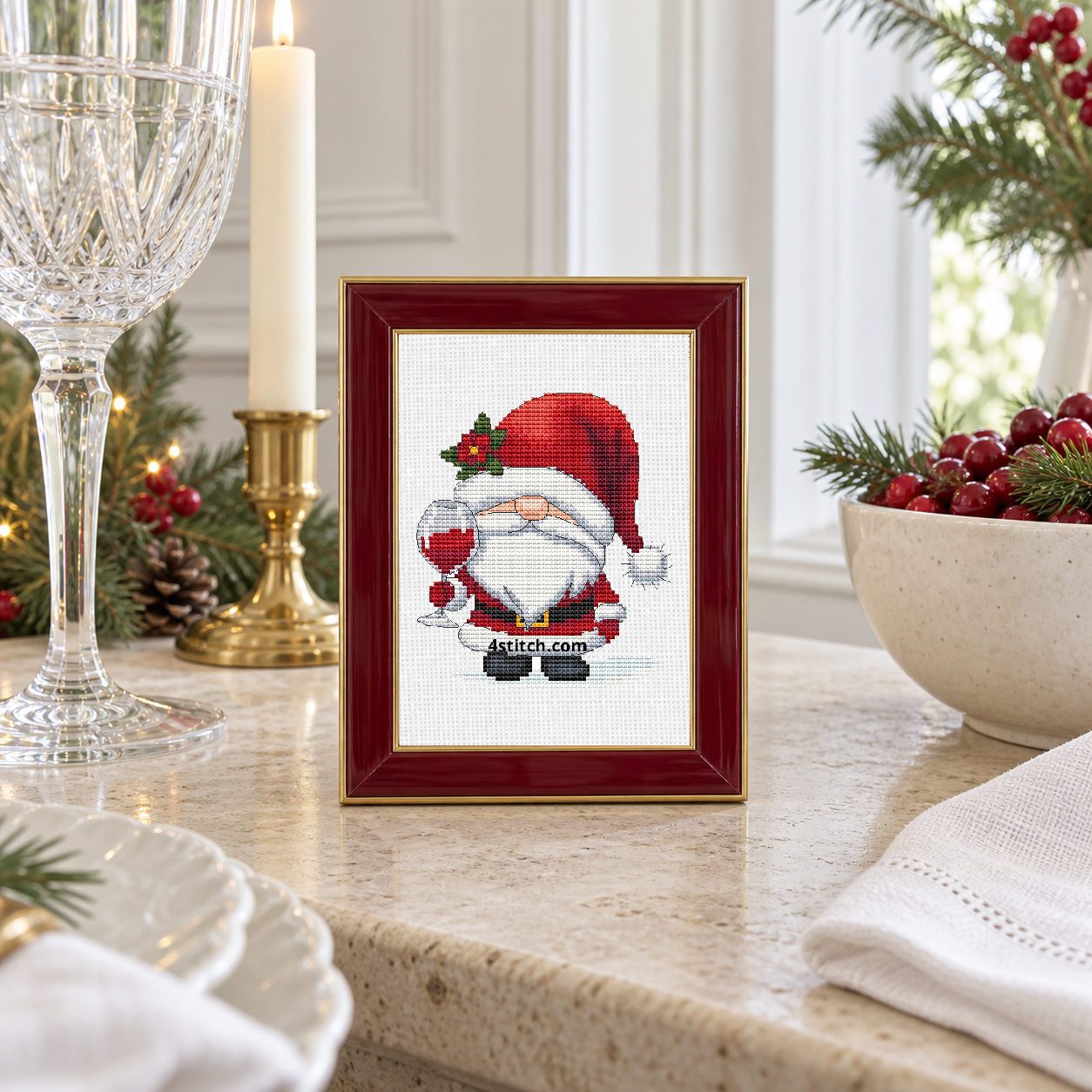 Wine Glass Santa Gnome with a red Santa hat with holly and a stemmed glass of red wine, on white Aida in a burgundy-and-gold frame on a bright Christmas dining console.