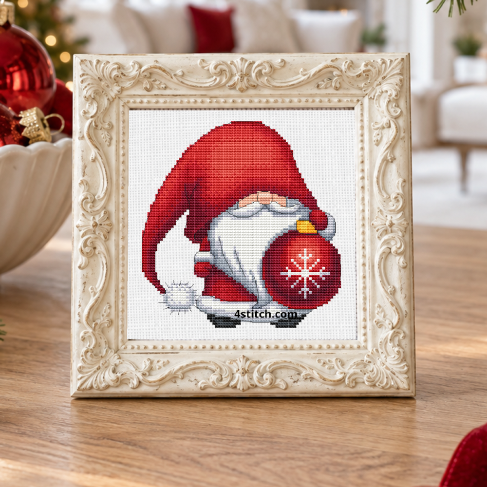 Close-up of Red Snowflake Bauble Gnome on white Aida in an ivory frame on a bright Christmas ornament-sorting table.