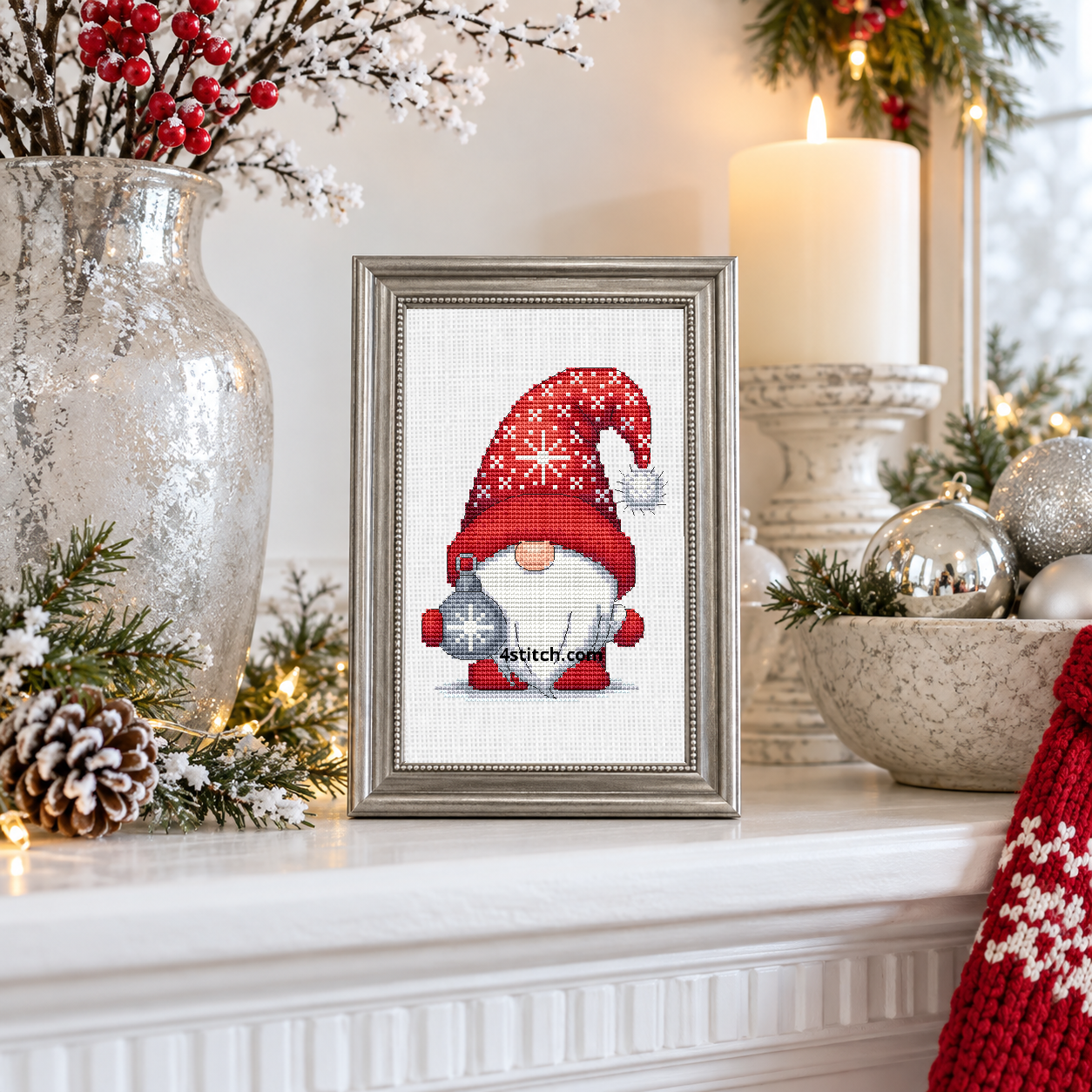 Wider interior view of Silver Snowflake Bauble Gnome on white Aida in a pewter-silver frame on a bright white winter mantel, with the small frame resting among coordinating Christmas decorations.