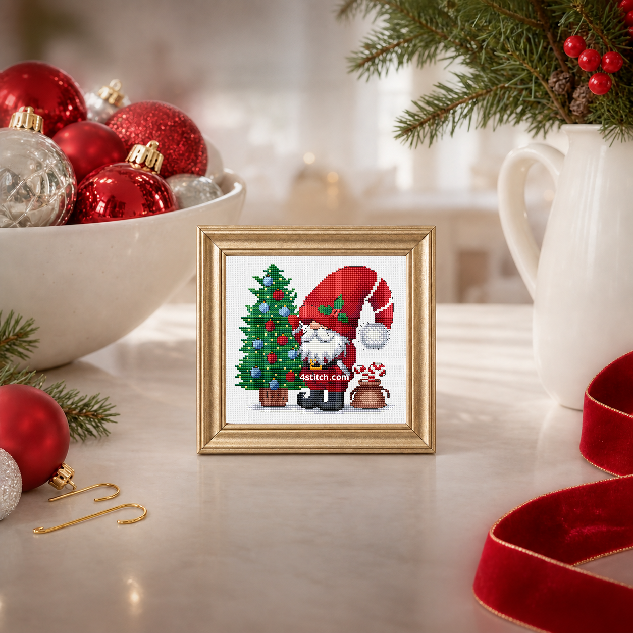 Wider interior view of Christmas Tree Ornaments Gnome on white Aida in a champagne-gold frame on a luminous ornament-sorting table, with the small frame resting among coordinating Christmas decorations.