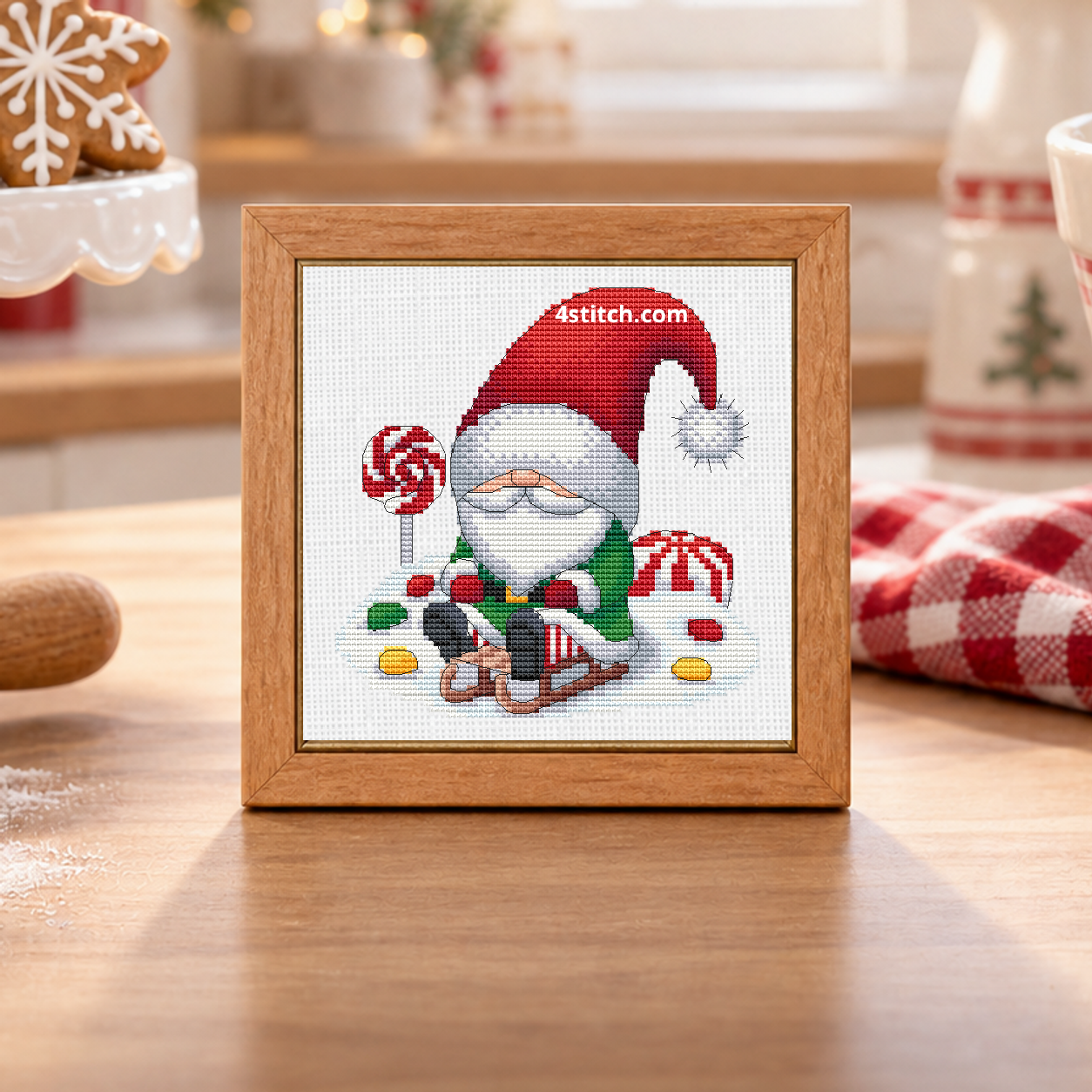 Close-up of Gingerbread Sleigh Christmas Gnome on white Aida in a warm maple frame on a bright Christmas baking bench.