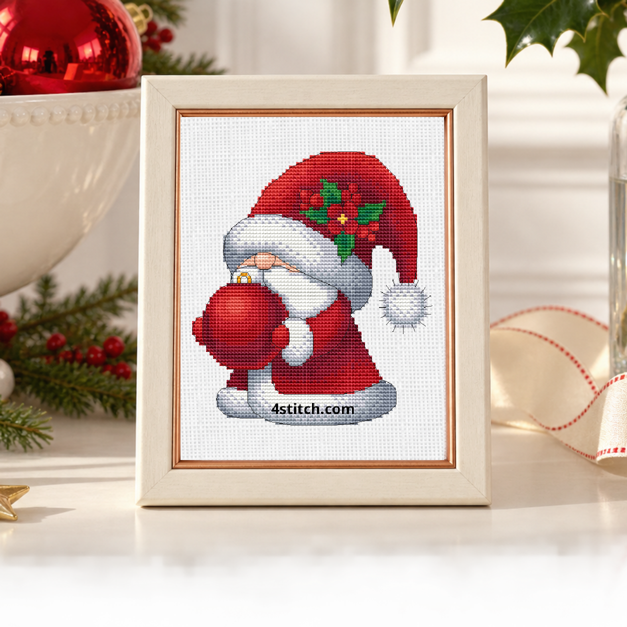 Close-up of Holly Bauble Santa Gnome on white Aida in an ivory frame with a copper lip on a bright ornament display.