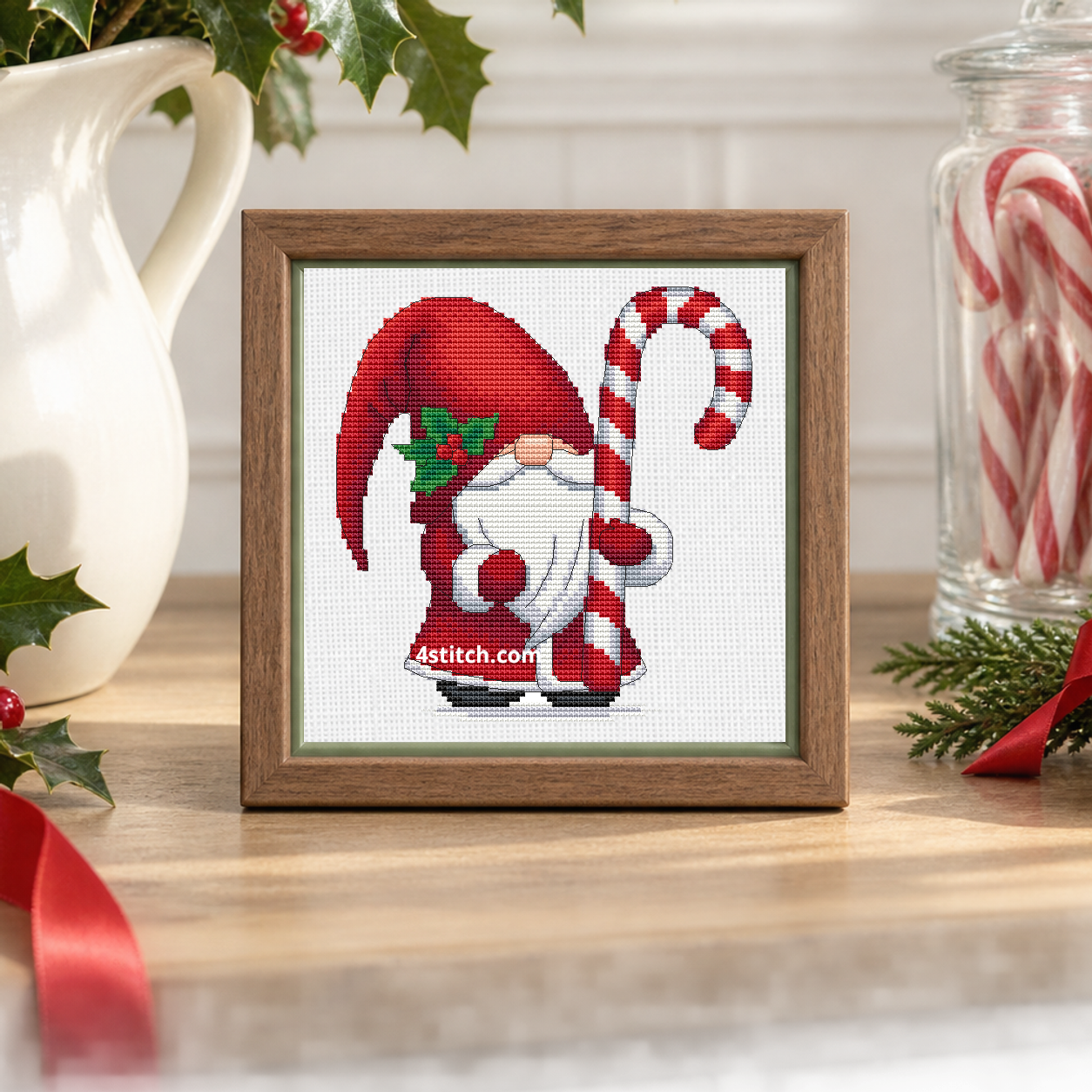 Close-up of Holly Candy Cane Gnome on white Aida in a light walnut frame on a cheerful holly-decorated console.