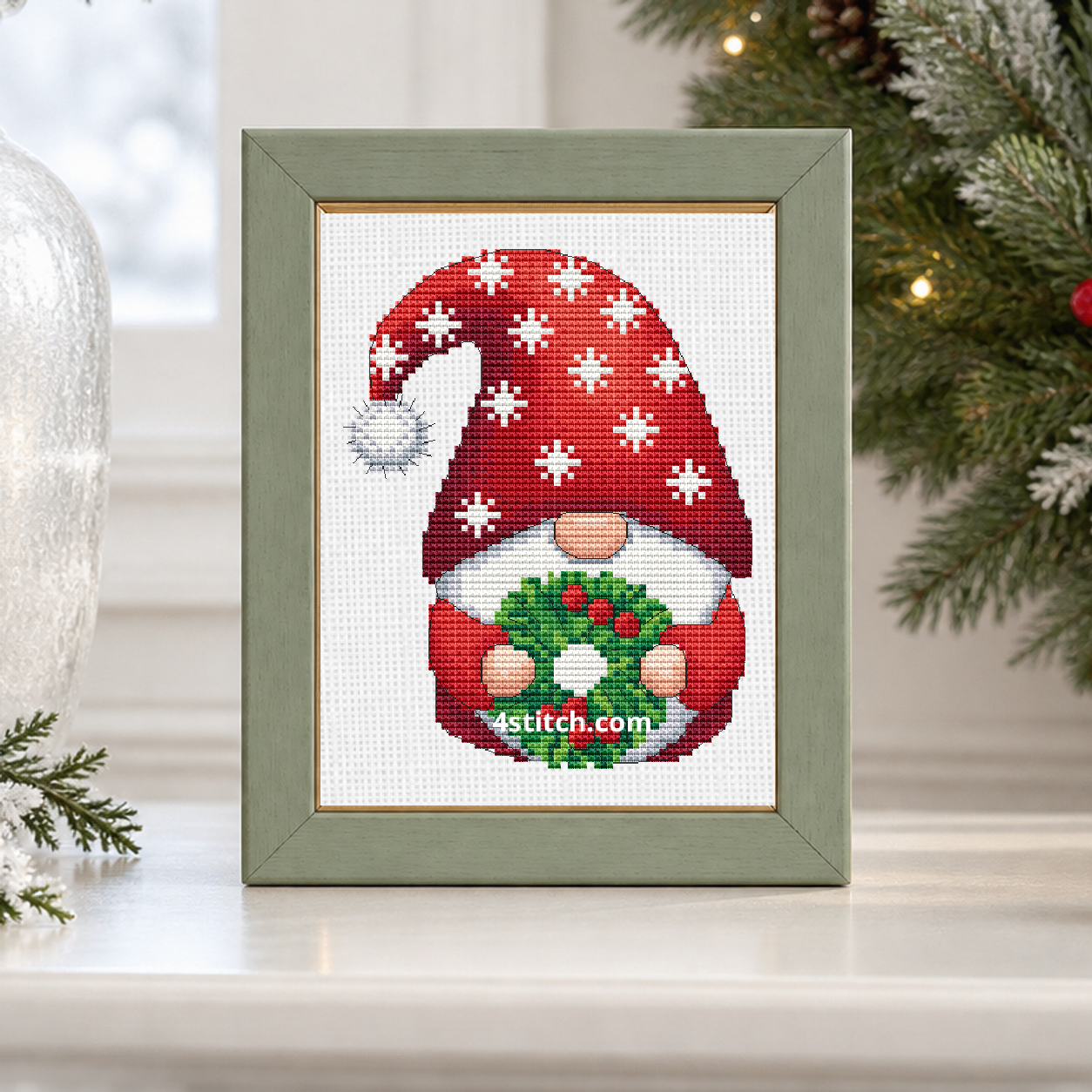 Close-up of Snowflake Wreath Christmas Gnome on white Aida in a soft sage-and-gold frame on a luminous winter mantel.