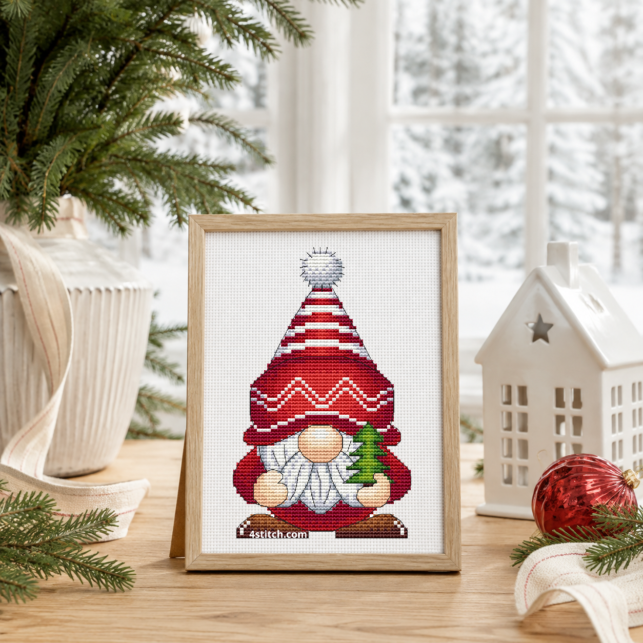 Mini Christmas Tree Gnome with a miniature fir tree and a tall red-and-white patterned hat, on white Aida in a blond oak frame beside a potted fir and a white ceramic Christmas house.