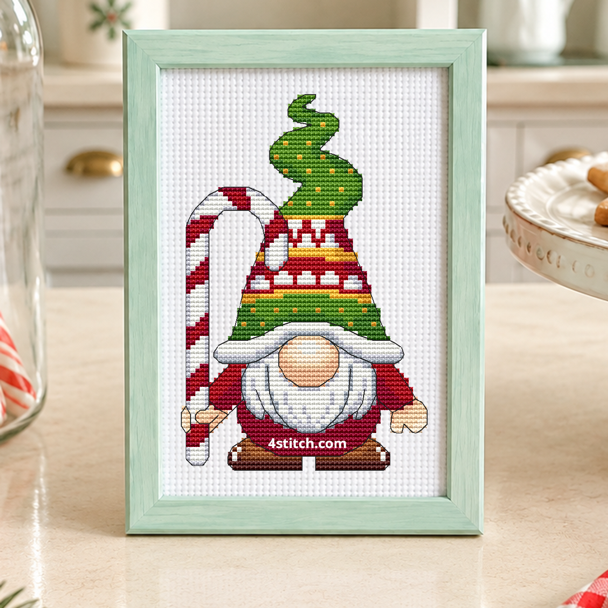 Candy Cane Tree Hat Gnome with a red-and-white candy cane and a curling green Christmas-tree hat, on white Aida in a mint green frame in a bright Christmas bakery with candy canes and star biscuits.