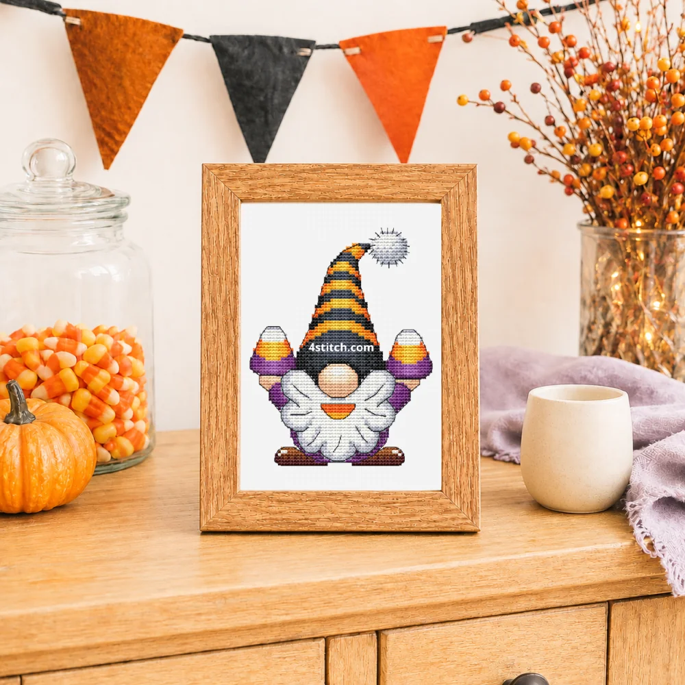 Small framed Candy Corn Halloween Gnome cross stitch on white Aida in a bright candy-corn Halloween tabletop interior