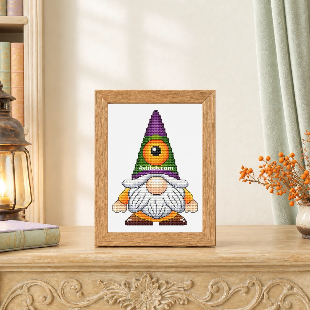 Small framed Cyclops Halloween Gnome cross stitch on white Aida standing on a light carved sideboard in a bright autumn interior