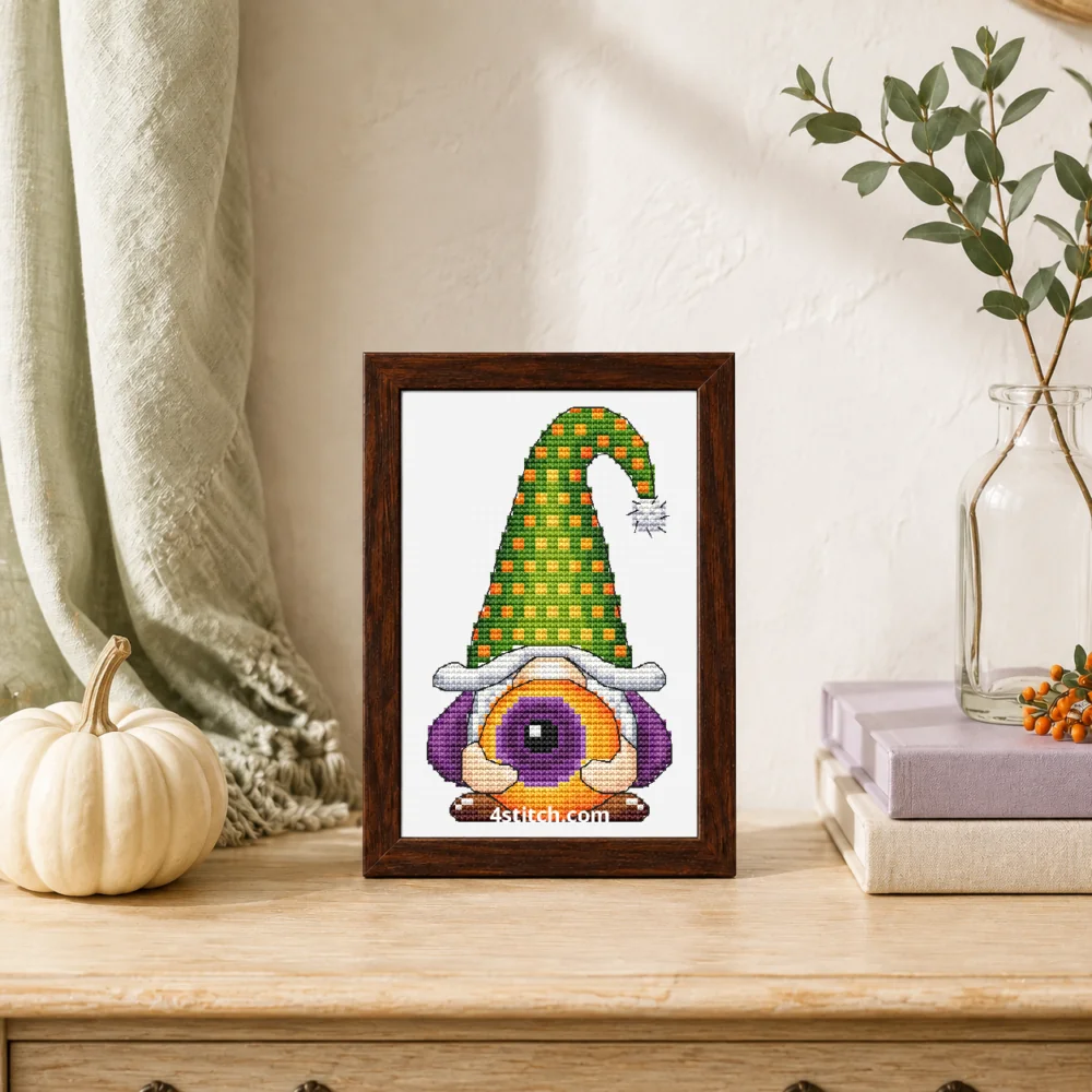 Small framed Eyeball Hat Halloween Gnome cross stitch on white Aida standing on a light wood console in a bright autumn interior