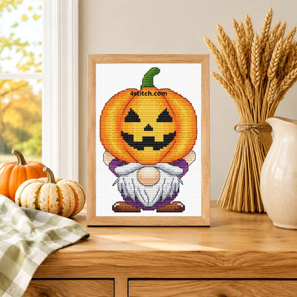 Small framed Pumpkin-Carrying Halloween Gnome cross stitch on natural white Aida standing on a light wood table in a bright harvest interior