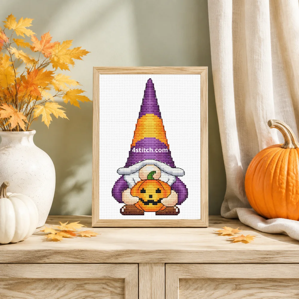 Small framed Pumpkin Hug Halloween Gnome cross stitch on natural white Aida standing on a light console in a bright harvest interior