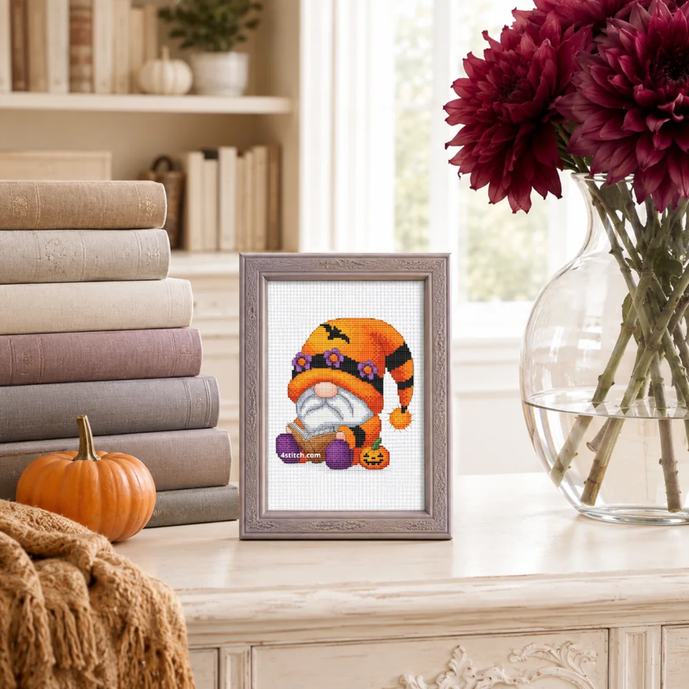 Small framed Pumpkin Flower Hat Gnome on white Aida in a bright themed interior, with the complete original motif and its 4stitch.com watermark.
