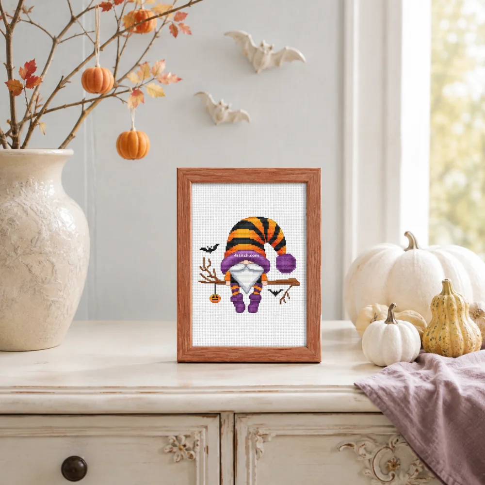 Small framed Pumpkin Charm Branch Halloween Gnome on white Aida in a bright themed interior, with the complete original motif and its 4stitch.com watermark.