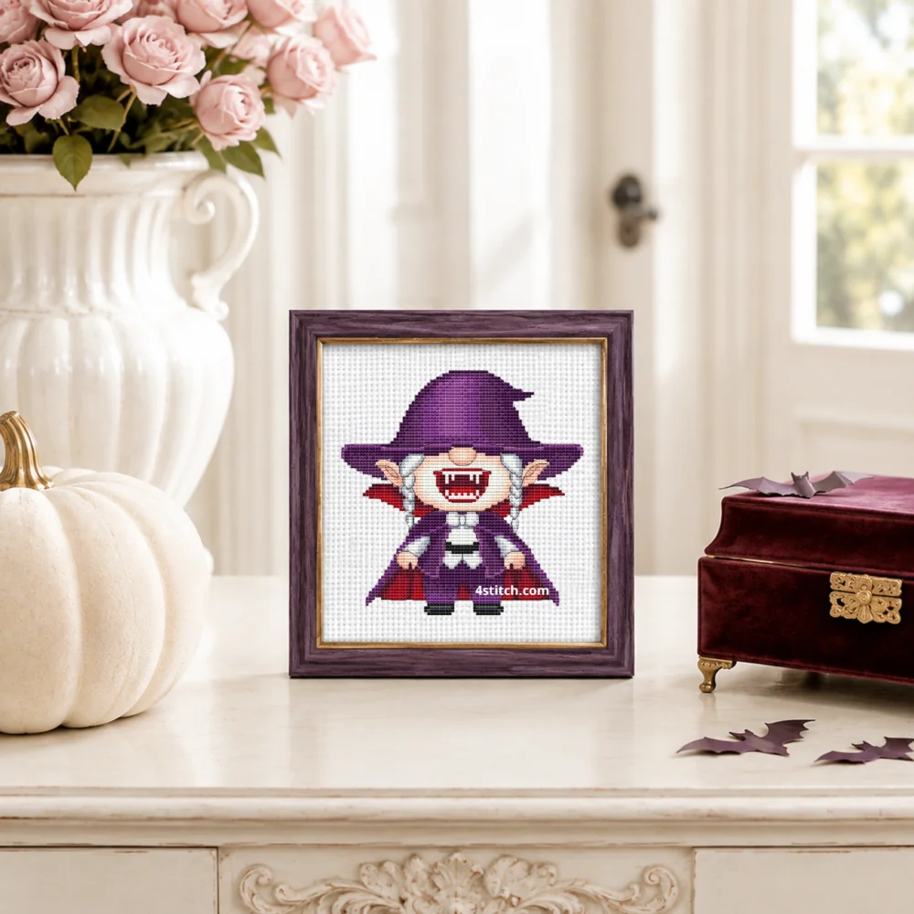 Vampire Halloween Gnome Cross Stitch Pattern shown as a small framed embroidery on white Aida in a bright Halloween interior.