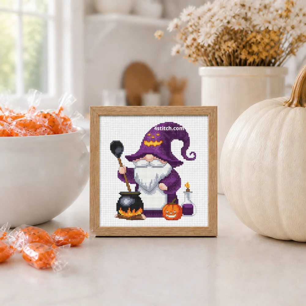 Cauldron Witch Gnome Cross Stitch Pattern shown as a small framed embroidery on white Aida in a bright Halloween interior.