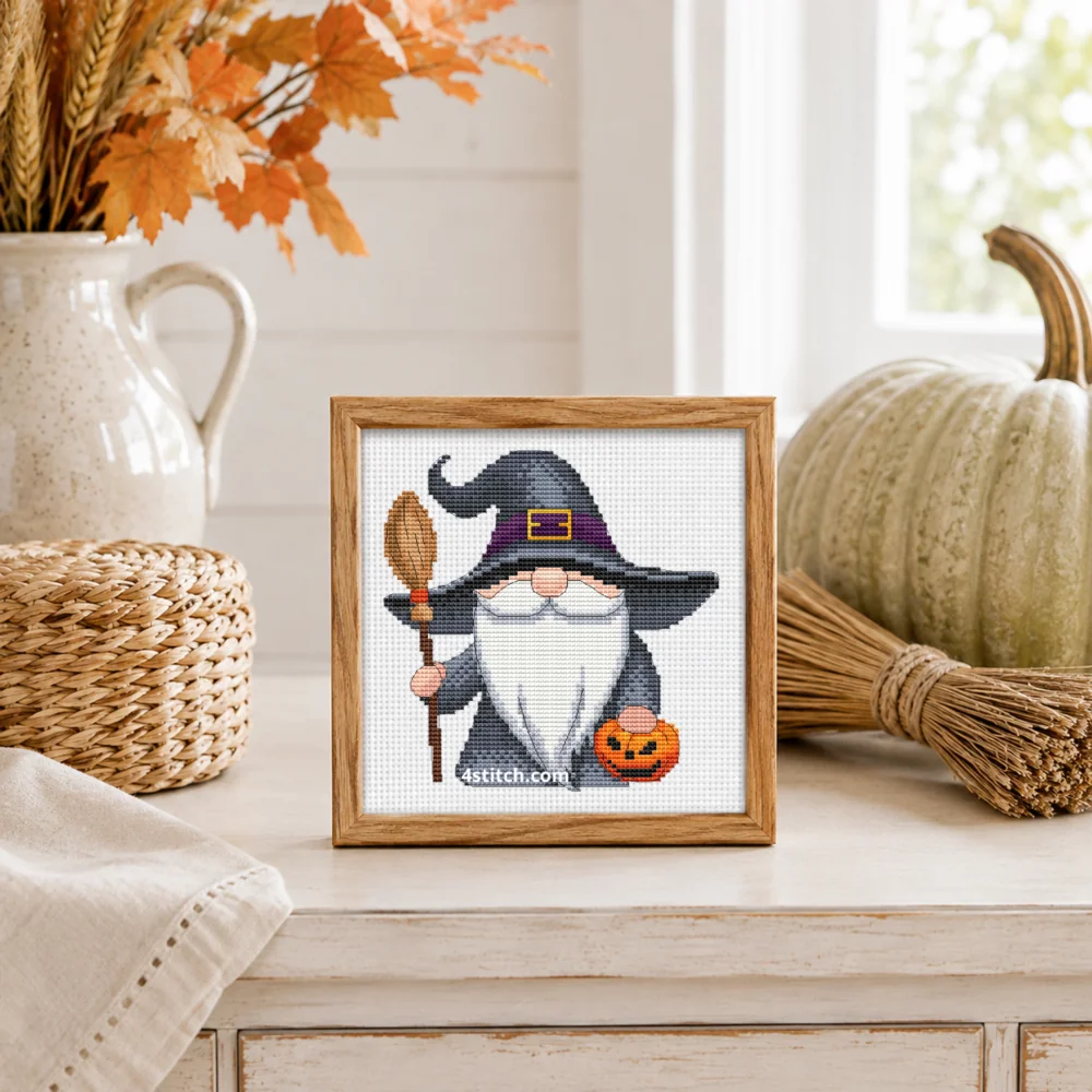Broom and Pumpkin Witch Gnome Cross Stitch Pattern shown as a small framed embroidery on white Aida in a bright Halloween interior.