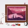 A cross stitch pattern of a pink and orange sunrise over a mountain range, with silhouetted trees in the foreground.